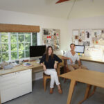 Kalon Studios co-founders Michaele Simmering and Johann Pauwen seated at their light-filled, modern wooden desks in their design studio.