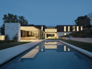 Exterior view of Feldman Architecture's Guzhai biophilic home at dusk, showcasing a tranquil swimming pool reflecting the brightly lit open-plan living areas and outdoor dining patio.
