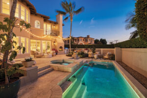 Exterior view of the European-inspired villa at 1000 Highview Avenue, Manhattan Beach, showcasing a large illuminated swimming pool, spa, outdoor fireplace, and stylish seating areas on a spacious patio at twilight.