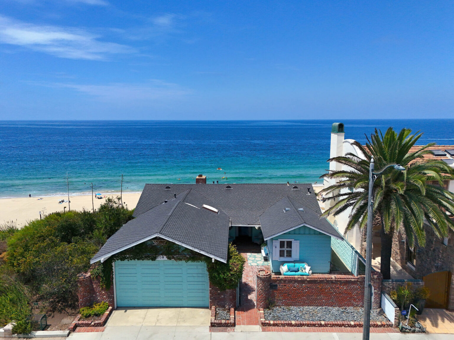 An aerial view of the historic Tiffany-blue beach cottage at 809 Esplanade in Redondo Beach, situated right on the oceanfront with the blue sea in the background.