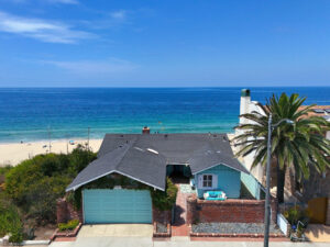 An aerial view of the historic Tiffany-blue beach cottage at 809 Esplanade in Redondo Beach, situated right on the oceanfront with the blue sea in the background.