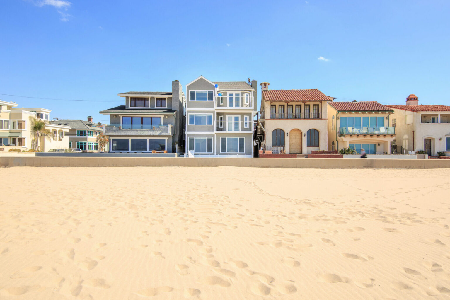 A wide sandy beach leading to a row of oceanfront homes along The Strand in Hermosa Beach, featuring the three-story property at 1836 The Strand.