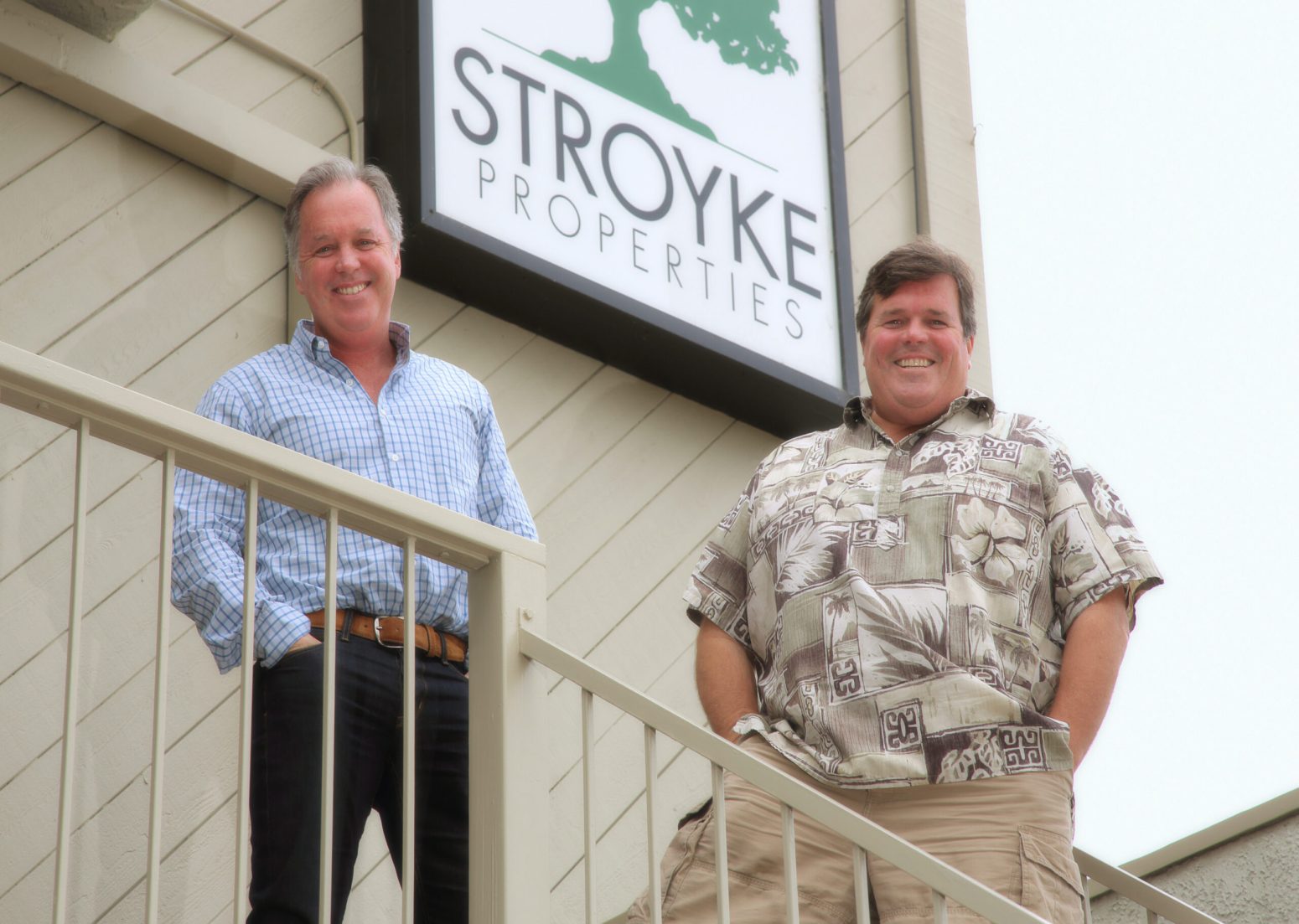 Bryn Stroyke (left) and Robb Stroyke (right) smiling on a balcony in front of their Stroyke Properties sign, introducing the article about their business.