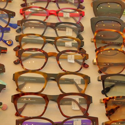 A close-up view of numerous eyeglasses and sunglasses, featuring diverse frames and colors, displayed in neat rows at Eyedentity Optique. Many frames are labeled Anne et Valentin.