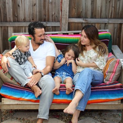 Ben and Shannon Watkins, marlowe+jay founders, relaxing with their two young children on a wooden bench adorned with colorful, nature-inspired textiles. This image introduces the creative family behind the brand.