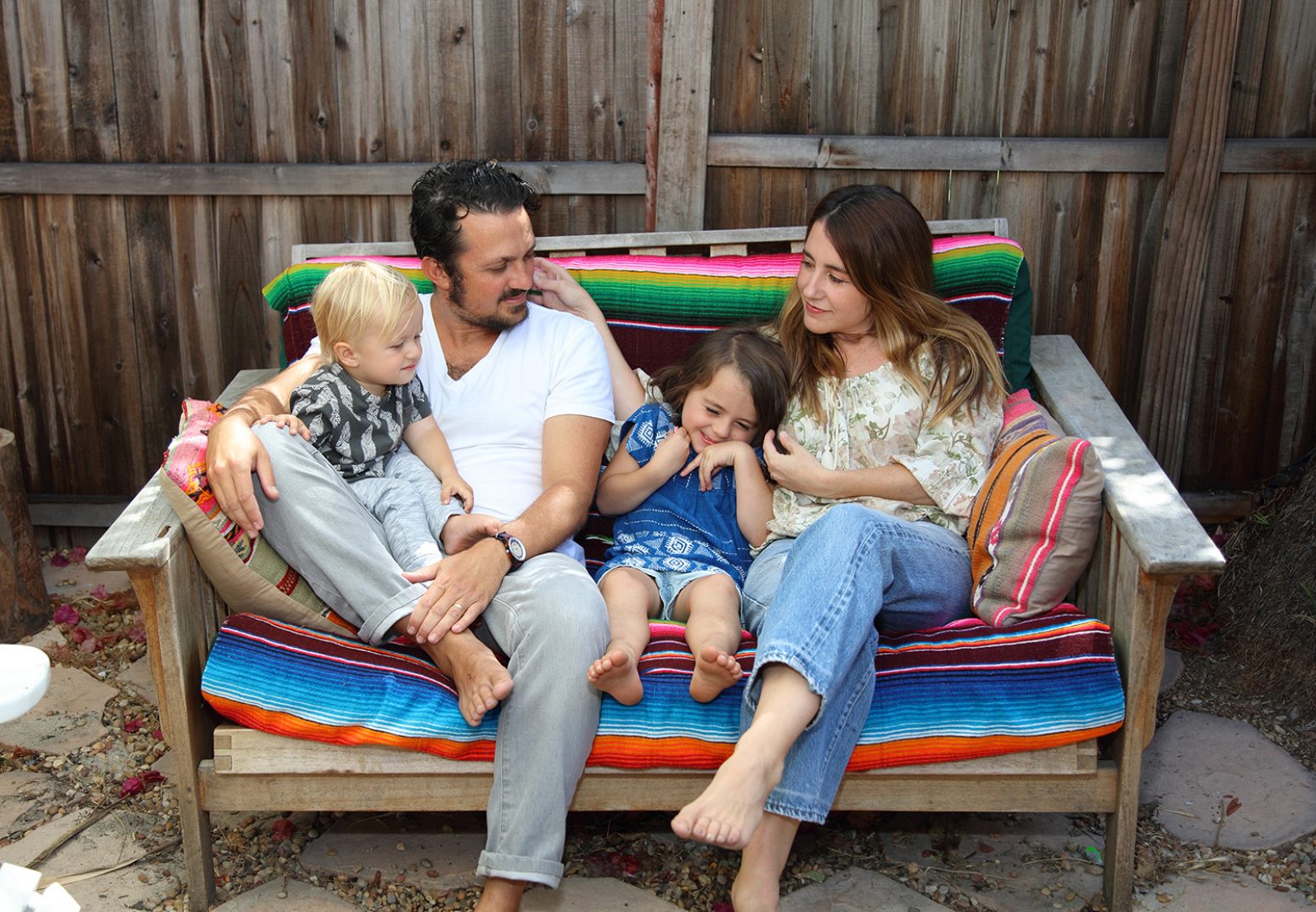 Ben and Shannon Watkins, marlowe+jay founders, relaxing with their two young children on a wooden bench adorned with colorful, nature-inspired textiles. This image introduces the creative family behind the brand.