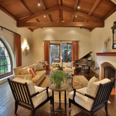 Full view of the spacious living room in Benny Goodman's former Spanish-style home, featuring a grand piano, fireplace, beamed ceiling, and large windows. This image is part of a real estate gallery.