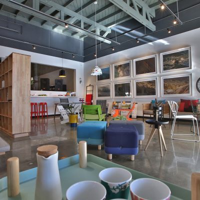 Interior view of Hermosa Design showroom featuring contemporary furniture, framed artwork, a wooden bookshelf, and industrial ceiling details, representing the brand's aesthetic.