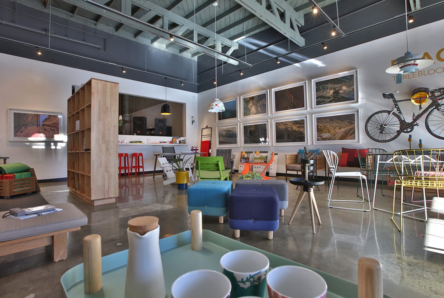 Interior view of Hermosa Design showroom featuring contemporary furniture, framed artwork, a wooden bookshelf, and industrial ceiling details, representing the brand's aesthetic.