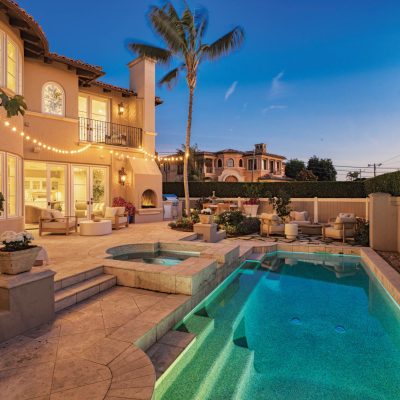 Exterior view of the European-inspired villa at 1000 Highview Avenue, Manhattan Beach, showcasing a large illuminated swimming pool, spa, outdoor fireplace, and stylish seating areas on a spacious patio at twilight.