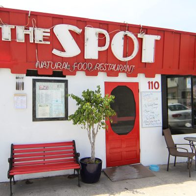 The exterior of The Spot Natural Food Restaurant in Hermosa Beach, showing its iconic red awning, main entrance, outdoor seating, and menu, serving as an identifying visual for the article.