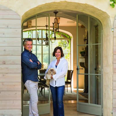 Portrait of mid 40's caucasian male-female couple in stone archway looking into dining area of home.